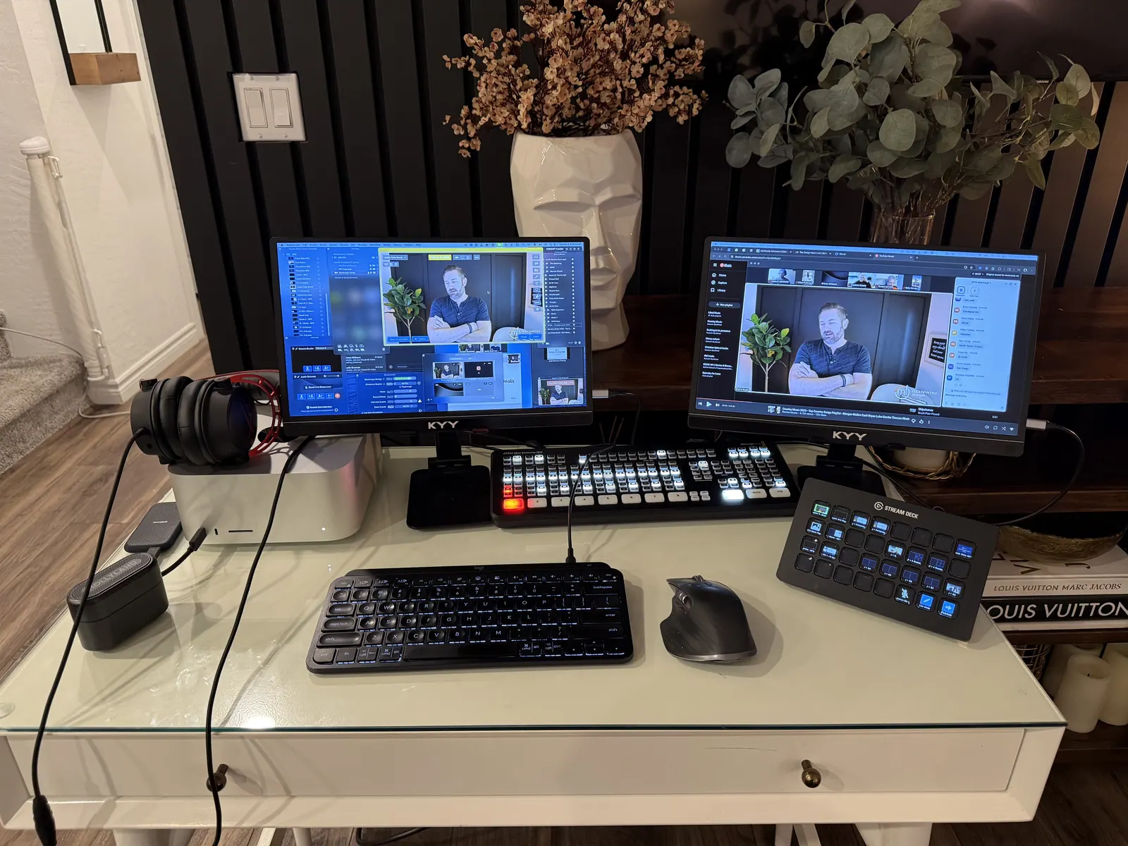 Home production desk: two monitors, a video switcher, a Stream Deck, and a guest live on screen